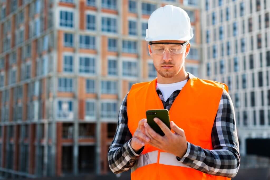 Ouvrier du bâtiment utilisant une application mobile sur un chantier pour gérer les opérations et les projets de construction.